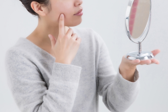 鏡の前で自分の顔（肌）を確認する女性