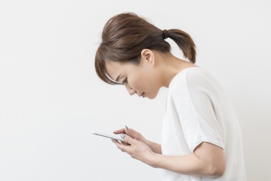 頭・首・肩・背中に負担のかかる姿勢でスマホ（スマートフォン）を操作している女性