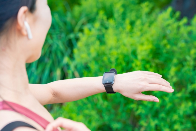 屋外で、手元のスマートウォッチを確認するスポーツウエア姿の女性