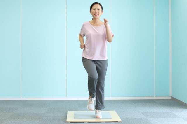 屋内で有酸素運動をする女性（ステップボードで足踏み、軽いウォーキング、足上げ運動）